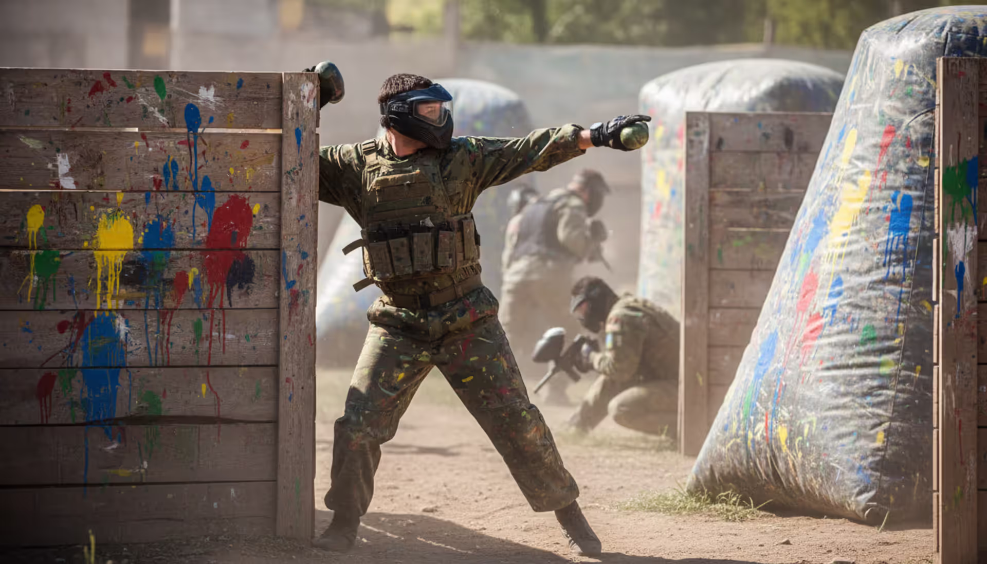 Paintball player in full gear throwing a paint grenade from behind a wooden barricade on an outdoor field