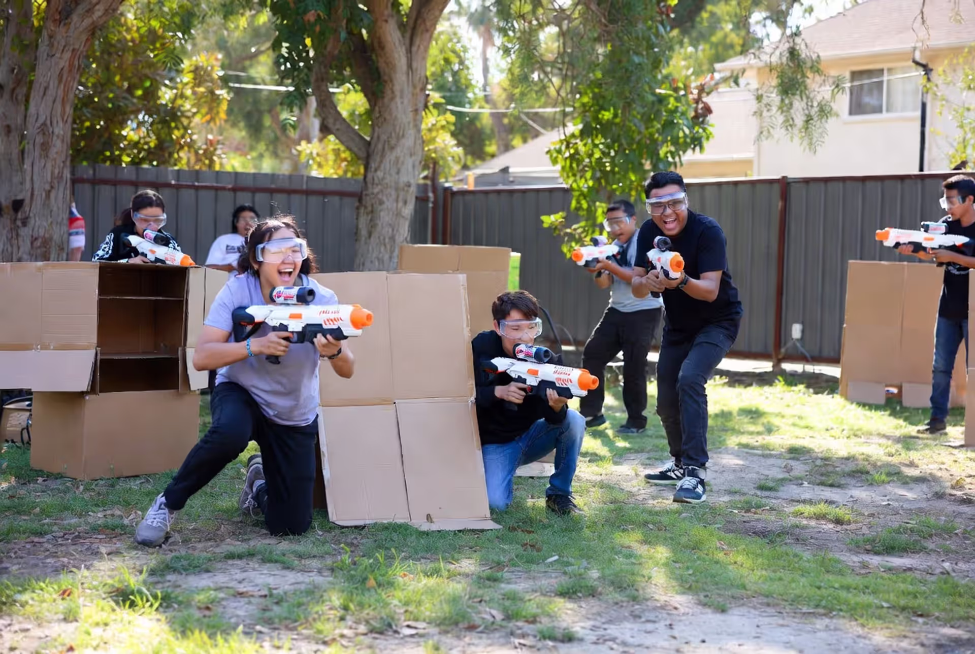 People playing gel blaster game in backyard wearing protective goggles